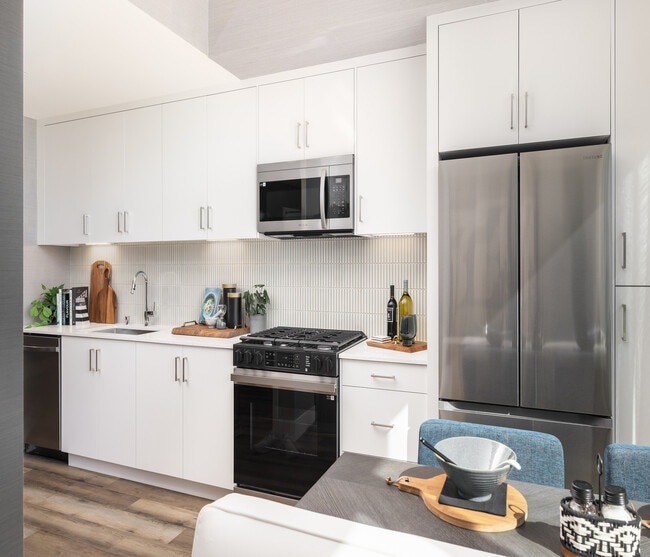 Bright, modern kitchen with sleek stainless steel appliances, abundant white cabinetry, and stylish wood flooring. Perfect for culinary creativity. - Ancora Apartments