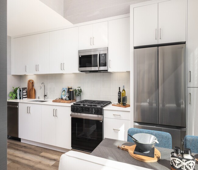 Cocina moderna y luminosa con elegantes electrodomésticos de acero inoxidable, abundantes gabinetes blancos y elegantes pisos de madera. Perfecta para la creatividad culinaria. - Ancora Apartments