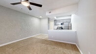 This single-floor unit presents a thoughtfully designed open-concept layout that seamlessly connects the living area to the kitchen. The living space is finished with warm, plush carpeting and textured walls in a soft neutral palette, creating a comfortable and inviting atmosphere. A ceiling fan overhead ensures year-round comfort, while a window fitted with horizontal blinds allows natural light to filter into the space.

The kitchen is a standout feature, showcasing gray shaker-style cabinetry, crisp white quartz countertops, and a classic white subway tile backsplash. Stainless steel appliances — including a refrigerator, range with coil burners, over-the-range microwave, and dishwasher — provide a polished, functional cooking environment. Light wood-look flooring runs throughout the kitchen, contrasting neatly with the carpeted living area. A peninsula counter with a built-in sink opens toward the living room, enhancing the open flow of the space.

The entry area features the same plush carpeting, a clean white paneled door, and a textured ceiling, maintaining a consistent and cohesive design language across the unit. Overall, the space offers a well-maintained, move-in-ready environment with modern finishes and a bright, airy feel.