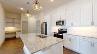 This single-floor residence showcases a clean, contemporary design highlighted by wood-look flooring, crisp white walls, and an abundance of natural light throughout. The open-concept kitchen serves as the centerpiece of the living area, featuring a large island with a granite countertop, an undermount stainless steel sink, and a high-arc faucet. White shaker-style cabinetry extends to the ceiling, complemented by a subway tile backsplash and a full suite of stainless steel appliances, including a refrigerator, range, microwave, and dishwasher. Geometric gold pendant lights add a modern decorative touch above the island.

The kitchen flows seamlessly into a spacious living area, where a ceiling fan, recessed lighting, and multiple windows create a bright, comfortable atmosphere. A built-in desk with cabinetry offers a dedicated workspace within the living space.

The bathrooms feature marble-style porcelain tile flooring and wall surrounds, with granite-topped vanities and gold-toned hardware. One bathroom includes a soaking tub, while another offers a glass-enclosed walk-in shower. A generously sized walk-in closet with multi-tiered shelving and hanging rods provides ample storage. Bedrooms are well-proportioned with natural light from large windows.