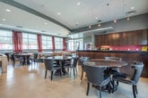 This contemporary amenity facility is thoughtfully designed to offer a diverse range of spaces for relaxation, work, and entertainment. The centerpiece is a dramatic double-height lounge, anchored by a sculptural curved ceiling installation and floor-to-ceiling windows dressed in bold red patterned curtains. Polished concrete floors with inlaid border details and a generous sectional sofa create an inviting atmosphere flooded with natural light.

Adjacent to the lounge is a dedicated business center featuring built-in workstations with multiple computers, bold red carpet, and a wall-mounted display screen. A separate conference room offers a live-edge wooden table, stylish blue upholstered chairs, and decorative patterned wall panels that lend an artistic touch.

A casual dining area showcases sleek black leather seating, round tables, a kitchenette counter with a pink glass tile backsplash, and sliding doors that open to an outdoor pool area. The game room is well-equipped with a billiards table, ping-pong table, and flat-screen television, all set against large windows with outdoor views.

A private theater room provides a tiered seating arrangement with plush white chairs and a bold red velvet sectional at the front, framed by floor-to-ceiling blackout curtains and a ceiling-mounted projector for an immersive cinematic experience.