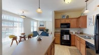 This single-floor residence offers a thoughtfully designed open-concept layout that seamlessly connects the kitchen, dining, and living areas. The kitchen is well-equipped with warm honey-toned cabinetry, light countertops, black appliances including a range, over-the-range microwave, and dishwasher, complemented by light hardwood-style flooring. A large center island provides additional prep and casual dining space. The open living room features plush carpeting, generous natural light from multiple windows, and a cozy fireplace, creating a welcoming atmosphere. A separate dining nook benefits from a full-height sliding glass door with vertical blinds, filling the space with natural light. The bedrooms are carpeted and bright, each featuring windows with blinds, neutral tones, and ample room for furnishings. The primary bedroom includes access to a private bathroom outfitted with a dual-sink vanity, warm wood cabinetry, tile flooring, and a walk-in closet. A dedicated laundry room houses a full-size washer and dryer with an overhead utility shelf, adding everyday convenience. Throughout the residence, light-toned walls, wood trim details, and consistent finishes create a cohesive and comfortable living environment.