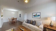 This single-floor residence offers a thoughtfully designed layout that balances comfort and functionality. The living area is an inviting space anchored by a neutral-toned sofa accented with patterned pillows, a herringbone-patterned coffee table, and a vibrant cityscape artwork on the wall. Large windows flood the room with natural light and provide views of surrounding greenery. The adjoining dining area features an elegant round wood table beneath a modern chandelier, complemented by crown molding and consistent wood-style flooring that runs throughout the home.

The kitchen is well-equipped with stainless steel appliances, including a gas range, built-in microwave, and French door refrigerator. Taupe-toned shaker cabinetry pairs with light quartz countertops, offering ample storage and workspace. An arched passageway connects the kitchen to the main living spaces, adding an architectural detail that enhances the overall flow.

Two comfortable bedrooms each feature windows with natural views and soft, neutral color palettes. The bathroom is finished with a wide vanity, white quartz countertop, full-width mirror, and a tub-shower combination. A dedicated laundry area with a full-size washer and dryer and overhead wire shelving adds practical convenience to the home.