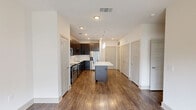 Located at 1851 Knightsbridge Rd in Farmers Branch, TX, this one-bedroom, one-bathroom residence offers a well-designed single-floor layout that maximizes every inch of its living space. The open-concept kitchen serves as the heart of the home, showcasing rich dark-espresso cabinetry, a classic tile backsplash, and a full suite of stainless steel appliances including a range, microwave, dishwasher, and French door refrigerator. A generously sized center island with a crisp white countertop provides additional prep space and casual seating, while stylish pendant lighting adds a modern touch overhead. Hardwood-style flooring flows throughout the main living and kitchen areas, complementing the bright, neutral color palette. The living area benefits from large sliding glass doors that invite natural light and outdoor views. The bedroom is carpeted for comfort and features a ceiling fan, a window with outdoor views, and direct access to a walk-in closet outfitted with multiple hanging rods and shelving. The bathroom includes a tub-shower combination with tiled surround and hardwood-style flooring that ties the space together cohesively. Clean lines, recessed lighting, and a contemporary design aesthetic give this residence a polished, move-in-ready appeal.