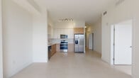 Located at 1839 NW 17th Ave in Miami, FL, this single-floor residence showcases a modern, minimalist design with a bright, neutral palette carried throughout every room. The open-concept kitchen is a standout feature, outfitted with a two-tone cabinetry scheme pairing white upper cabinets with warm natural wood lower cabinets, a white subway tile backsplash, a stainless steel appliance suite including a side-by-side refrigerator with ice dispenser, electric range, over-the-range microwave, and dishwasher, all set atop large-format light-toned tile flooring that extends into the living areas. A hallway with louvered closet doors connects the main living spaces to the private quarters, where the bedrooms feature clean white walls and ample natural light. One bedroom includes light wood-toned flooring and a sliding closet, while another benefits from a window with city views and tile flooring. The bathrooms are thoughtfully appointed with natural wood vanities, white quartz countertops, and white tile work. The primary bath includes a glass-enclosed walk-in shower with floor-to-ceiling white tile, while a secondary bath features a lighted vanity mirror with brushed gold fixtures, adding a refined touch to the overall clean, contemporary aesthetic.