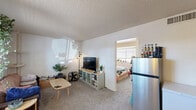 Located on East Route 66 in Flagstaff, Arizona, this efficient one-bedroom, one-bathroom unit offers a practical and well-organized single-floor layout. The living room serves as the central gathering space, featuring wall-to-wall carpeting, a textured ceiling, and a bright window fitted with blinds that allows natural light to filter in and cast warm patterns across the white walls. The open sightline from the living area into the adjacent kitchen zone provides a sense of connectivity, with tile flooring marking the transition into the kitchen space, which includes a stainless steel refrigerator and storage cabinetry. A partial wall divider separates the living and bedroom areas while maintaining an open, airy feel throughout. The bedroom is a generously proportioned private retreat relative to the overall footprint of the unit, featuring carpet flooring, a textured ceiling, and a window with a built-in sill — ideal for plants or décor — that brings in ample natural light. The white walls throughout keep the interior feeling bright and clean. Overall, this unit delivers a straightforward and functional layout well-suited for individuals or couples seeking a cozy, easy-to-maintain space in Flagstaff.