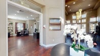 This single-floor amenity space combines elegance and functionality across a thoughtfully designed layout. The grand lounge is an immediate standout, boasting soaring double-height ceilings, an expansive curved wall of plantation-shuttered windows that flood the room with natural light, and rich hardwood flooring that runs throughout much of the facility. Decorative wall moldings and curated artwork add a refined aesthetic to the welcoming reception and lounge areas, which also feature built-in cabinetry with granite countertops and a wall-mounted display screen.

A private office area offers a polished workspace with a dark wood desk, guest seating, built-in shelving, and natural light filtering through slatted blinds. Adjacent to this is a cozy reading nook with a leather armchair, built-in bookshelves, and plantation shutters offering views to the outdoors.

The fitness wing is well-equipped, housing a primary gym room with cardio machines including treadmills, ellipticals, and steppers, accented by large framed mirrors and textured grasscloth walls. A dedicated spin studio features a row of ICG stationary bikes in a clean, minimalist setting. Carpeted corridors with warm grasscloth wall treatments connect the various wings, lending a cohesive and polished feel throughout the entire space.