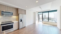 Located in the heart of San Diego's East Village at 310 A St, this modern single-floor residence showcases a clean, contemporary design with an open and airy floor plan. Warm hardwood flooring flows throughout the main living areas, complemented by crisp white walls and recessed and track lighting that illuminate the space efficiently.

The living area is anchored by expansive floor-to-ceiling windows and a glass-railed balcony, flooding the interior with natural light and offering striking views of the San Diego skyline. The seamless transition between the living and kitchen areas creates an inviting, open feel ideal for both everyday living and entertaining.

The kitchen is outfitted with flat-front cabinetry in a light wood finish, white quartz countertops, a marble-style tile backsplash, and a full suite of stainless steel appliances, including a refrigerator, range, microwave, and dishwasher. Under-cabinet lighting adds both functionality and ambiance.

The bathroom continues the refined aesthetic with large-format white marble-look tile on both the floors and the tub surround, paired with a soaking tub and light wood vanity cabinetry. The overall design palette throughout the residence is cohesive and understated, prioritizing clean lines, quality materials, and a bright, welcoming atmosphere that reflects the best of modern urban living in downtown San Diego.
