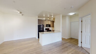 This single-floor residence is designed with an open-concept layout that connects the kitchen, dining, and living areas into one cohesive space. The kitchen serves as a central focal point, featuring a peninsula with granite countertops and an integrated sink, offering both additional workspace and a natural division between the cooking and living areas. Dark espresso-toned cabinetry provides ample storage, while black appliances—including a refrigerator, gas range, and microwave—add a consistent, modern aesthetic. Track lighting above the kitchen ensures the workspace is well illuminated.

Wood-look plank flooring extends throughout the main living areas, contributing a warm yet clean visual tone against the neutral white walls and white baseboards. The open living area is generously proportioned, with multiple doors leading to additional rooms and providing a functional flow throughout the unit.

The bedrooms are finished with soft wall-to-wall carpeting and each features a window with blinds, allowing natural light and outdoor views. The bathroom includes a full soaking tub with shower combo, a curved curtain rod, wood-look flooring, and dark cabinetry with granite countertops that echo the kitchen's finishes, maintaining a cohesive design throughout the space.
