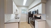 This single-floor residence offers a clean, contemporary aesthetic with light wood-style flooring and neutral gray tones carried consistently throughout. The galley-style kitchen is thoughtfully designed with white shaker cabinetry, quartz countertops, and a classic white subway tile backsplash. Stainless steel appliances — including a gas range, over-the-range microwave, and refrigerator — complete the space, while a skylight overhead floods the area with natural light. A window at the end of the kitchen provides a view of surrounding greenery, enhancing the bright and airy atmosphere.

The living area is generously proportioned, featuring large windows that invite natural light and offer leafy outdoor views. The entry door opens directly into this open space, making it feel welcoming and functional. A dedicated laundry closet within the unit houses a full-size washer and dryer alongside additional closet storage, adding significant everyday convenience.

The bedroom is well-sized with a large window framing a serene view of mature trees, creating a calm retreat. The bathroom features white shaker-style cabinetry, a single-basin vanity with a quartz-style countertop, a large mirror, and accessibility-friendly grab bar details. Light wood flooring extends through both rooms, tying the overall design together seamlessly.