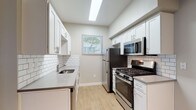 This single-floor residence offers a clean, contemporary aesthetic with light wood-style flooring and neutral gray tones carried consistently throughout. The galley-style kitchen is thoughtfully designed with white shaker cabinetry, quartz countertops, and a classic white subway tile backsplash. Stainless steel appliances — including a gas range, over-the-range microwave, and refrigerator — complete the space, while a skylight overhead floods the area with natural light. A window at the end of the kitchen provides a view of surrounding greenery, enhancing the bright and airy atmosphere.

The living area is generously proportioned, featuring large windows that invite natural light and offer leafy outdoor views. The entry door opens directly into this open space, making it feel welcoming and functional. A dedicated laundry closet within the unit houses a full-size washer and dryer alongside additional closet storage, adding significant everyday convenience.

The bedroom is well-sized with a large window framing a serene view of mature trees, creating a calm retreat. The bathroom features white shaker-style cabinetry, a single-basin vanity with a quartz-style countertop, a large mirror, and accessibility-friendly grab bar details. Light wood flooring extends through both rooms, tying the overall design together seamlessly.