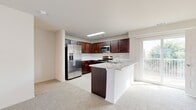 This two-story residence offers a thoughtfully organized layout across two floors, combining functional design with comfortable living spaces. The main level features an open-concept kitchen and living area, where the kitchen stands out with rich dark wood cabinetry, stainless steel appliances including a French door refrigerator, a built-in microwave, and an electric range. A peninsula with a marble-style countertop provides additional prep space and casual seating. A skylight adds natural brightness to the kitchen, while a sliding glass door connects the living area to an outdoor balcony. Plush neutral carpeting flows throughout the living spaces, complementing the clean white walls.

A carpeted staircase leads to the upper level, which houses both bedrooms, including a generously sized primary bedroom featuring vaulted ceilings, a ceiling fan, and a walk-in closet with wire shelving. The second bedroom also includes a ceiling fan and access to natural light. Three bathrooms are distributed across both floors, each finished with tile flooring, dark wood vanities, marble-style countertops, and well-lit mirrors. The overall aesthetic is clean and neutral, offering a move-in ready canvas with consistent finishes throughout.