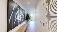 This well-appointed one-bedroom, one-bathroom residence offers a seamless blend of contemporary design and urban sophistication. The entry hallway sets the tone immediately, featuring light hardwood flooring, recessed lighting, and a striking large-scale graffiti-style artwork that makes a bold first impression alongside a stylish bench and lush indoor plant.

The open-plan kitchen and living area serves as the heart of the home. The kitchen is outfitted with sleek grey cabinetry extending to the ceiling, stainless steel appliances including a gas range and French door refrigerator, a dark tile backsplash, and an expansive white quartz waterfall island with bar seating — ideal for both cooking and casual dining. The living area flows naturally from the kitchen and is anchored by floor-to-ceiling glass walls that frame sweeping city skyline views and provide access to a private outdoor balcony, flooding the space with natural light.

The bedroom is a serene retreat, featuring its own floor-to-ceiling windows with city views, a rich dark accent wall, and light hardwood flooring. A dedicated closet provides practical storage. The bathroom is elegantly finished with large-format tile flooring, dark marble-clad walls surrounding the soaking tub and shower, a floating vanity, and pendant lighting, creating a spa-like atmosphere throughout.
