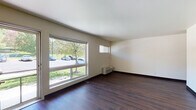 Located at 194 Tompkins Ave in Beacon, NY, this single-floor unit offers a straightforward and functional layout with consistent dark hardwood-style flooring running throughout the space. The main living area is open and well-lit, featuring a large picture window that invites abundant natural light and provides views of the surrounding greenery and streetscape. A second smaller window adds additional brightness, and a wall-mounted HVAC unit ensures climate control. A distinctive teal front door adds a touch of character to the entryway, which flows directly into the living space. The kitchen is compactly designed and positioned adjacent to the main living area. It is equipped with warm wood cabinetry, a coil-burner electric range, a full-size Whirlpool refrigerator, a wall-mounted ventilation fan, and ample counter space. An electrical panel is accessible from the living area near the hallway. The bathroom is clean and efficiently laid out, featuring a white vanity with a mirrored medicine cabinet, a standard toilet, and a full bathtub with shower fixtures. Neutral cream-toned walls throughout the unit provide a blank canvas for personalization. The space is practical and well-maintained, suited for single occupancy or a couple seeking a straightforward residence in the Beacon, NY area.