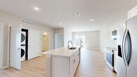 Located on Garland Avenue in Norwalk, Iowa, this well-appointed 2-bedroom, 1-bathroom residence offers a thoughtfully designed single-floor layout with modern finishes and a bright, open atmosphere. The combined kitchen and living area serves as the heart of the home, featuring light hardwood-style flooring, recessed lighting, and a vaulted ceiling that enhances the sense of space. The kitchen is equipped with stainless steel appliances — including a refrigerator with ice maker, electric range, and over-the-range microwave — complemented by crisp white shaker cabinetry and a large center island with an undermount sink and light countertops. Sliding glass doors in the living area open to a private balcony with neighborhood views, flooding the space with natural light. Both bedrooms are carpeted and include ceiling fans. The generously sized primary bedroom offers a walk-in closet with wire shelving systems, while the second bedroom is served by an additional closet with similar organization. The full bathroom features a tub-shower combination, toilet, and vanity with durable luxury vinyl plank flooring. An in-unit stacked laundry area adds everyday convenience to this clean, contemporary home.