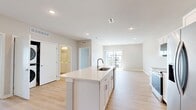 Located on Garland Avenue in Norwalk, Iowa, this well-appointed 2-bedroom, 1-bathroom residence offers a thoughtfully designed single-floor layout with modern finishes and a bright, open atmosphere. The combined kitchen and living area serves as the heart of the home, featuring light hardwood-style flooring, recessed lighting, and a vaulted ceiling that enhances the sense of space. The kitchen is equipped with stainless steel appliances — including a refrigerator with ice maker, electric range, and over-the-range microwave — complemented by crisp white shaker cabinetry and a large center island with an undermount sink and light countertops. Sliding glass doors in the living area open to a private balcony with neighborhood views, flooding the space with natural light. Both bedrooms are carpeted and include ceiling fans. The generously sized primary bedroom offers a walk-in closet with wire shelving systems, while the second bedroom is served by an additional closet with similar organization. The full bathroom features a tub-shower combination, toilet, and vanity with durable luxury vinyl plank flooring. An in-unit stacked laundry area adds everyday convenience to this clean, contemporary home.