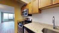 This single-floor residence features two bedrooms and two bathrooms, offering a practical and well-organized layout ideal for everyday living. The kitchen is a functional centerpiece of the home, equipped with stainless steel appliances including a gas range and an over-the-range microwave. Light wood cabinetry with sleek bar-pull hardware provides ample storage, while the granite-style countertops in soft cream and gold tones add a refined touch to the space. A stainless steel sink completes the kitchen setup. The warm, neutral wall tones throughout contribute to a cohesive and inviting ambiance. Natural light filters into the space, as evidenced by the glimpse of a glass door visible from the kitchen, suggesting an open and connected flow between the living areas. The hardwood-style flooring carries through the unit, adding warmth and continuity. With two full bathrooms serving the two bedrooms, this residence is designed with both comfort and convenience in mind, making it a well-rounded living space suited for a variety of lifestyles.