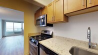 This single-floor residence features two bedrooms and two bathrooms, offering a practical and well-organized layout ideal for everyday living. The kitchen is a functional centerpiece of the home, equipped with stainless steel appliances including a gas range and an over-the-range microwave. Light wood cabinetry with sleek bar-pull hardware provides ample storage, while the granite-style countertops in soft cream and gold tones add a refined touch to the space. A stainless steel sink completes the kitchen setup. The warm, neutral wall tones throughout contribute to a cohesive and inviting ambiance. Natural light filters into the space, as evidenced by the glimpse of a glass door visible from the kitchen, suggesting an open and connected flow between the living areas. The hardwood-style flooring carries through the unit, adding warmth and continuity. With two full bathrooms serving the two bedrooms, this residence is designed with both comfort and convenience in mind, making it a well-rounded living space suited for a variety of lifestyles.