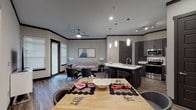 The Ivy presents a thoughtfully designed single-floor residence that seamlessly blends modern aesthetics with functional living. The open-concept layout connects the kitchen, dining, and living areas into one cohesive space, creating an inviting atmosphere ideal for both everyday living and entertaining.

The kitchen is a standout feature, equipped with dark charcoal cabinetry, stainless steel appliances including a range, over-the-range microwave, and refrigerator, complemented by crisp white quartz countertops and a classic subway tile backsplash. A central island with pendant lighting provides additional counter space and seating. Wood-look flooring flows throughout the main living areas, anchored by dark crown molding that adds a sophisticated contrast to the neutral walls.

The living area benefits from natural light through multiple windows fitted with white blinds, and includes a ceiling fan. A private exterior door adds convenient access. The bedroom offers a calm, carpeted retreat with ample natural light from a large window.

The bathroom is finished with large-format marble-look tile in the tub surround and flooring, paired with a white quartz vanity and dark cabinetry, delivering a clean, polished look consistent with the home's overall contemporary design.