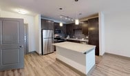 This single-floor residence in Grand Prairie, Texas, showcases a modern design aesthetic with thoughtfully selected finishes throughout. The kitchen serves as a central highlight, featuring rich dark espresso cabinetry that extends to the ceiling for maximum storage capacity. A central island with a granite countertop provides additional workspace and casual seating, illuminated by stylish pendant lighting overhead. Stainless steel appliances, including a refrigerator, range, and over-the-range microwave, complement the subway tile backsplash. Track lighting adds additional functionality to the kitchen space.

Light wood-look flooring flows throughout the main living areas, creating a cohesive and contemporary feel. The open-concept layout connects the kitchen to the living area, maximizing the sense of space and promoting ease of movement.

The bathroom is well-appointed with a granite-topped vanity, dark cabinetry with brushed nickel hardware, an undermount sink, and a large frameless mirror. Wood-look flooring continues into this space, maintaining design continuity.

A dedicated utility area includes built-in shelving and connections for laundry appliances, adding practical convenience. The overall palette of neutral whites and warm wood tones creates a clean, inviting ambiance throughout the residence.