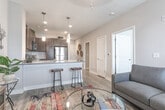 Located at 20 Libby St in Hampton, Virginia, this single-floor residence offers a well-designed layout that balances functionality and modern style throughout. The open-concept living and dining area is bright and welcoming, finished with wood-look plank flooring and anchored by a comfortable seating arrangement centered around a glass coffee table and a vibrant area rug. A private exterior door with large windows floods the space with natural light and provides direct outdoor access. The kitchen is thoughtfully appointed with rich dark-brown cabinetry, granite countertops, a tiled backsplash, stainless steel appliances including a range, microwave, dishwasher, and refrigerator, and a peninsula with bar seating illuminated by pendant lighting. The bedroom is a calm retreat featuring plush carpeting, a ceiling fan, and a generously sized window that invites ample daylight. It connects to a spacious walk-in closet outfitted with built-in shelving and hanging rods, offering excellent storage capacity. The bathroom continues the home's cohesive aesthetic with dark wood cabinetry, a granite-topped vanity, wood-look flooring, and a shower-tub combination. Neutral tones and consistent finishes throughout create a clean, contemporary ambiance suited for comfortable everyday living.
