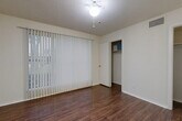 This single-floor unit offers a well-organized layout that maximizes its compact footprint. The main room features rich, dark hardwood-style flooring that runs throughout the space, neutral wall tones, and a textured ceiling with a ceiling fan and light fixture. A large floor-to-ceiling vertical blind-covered window fills the room with natural light and offers a pleasant outdoor view of green surroundings. Two closets provide ample storage, each with built-in shelving and hanging rods, conveniently accessible from the main living area. A bonus room adds flexibility to the layout and is equipped with a stainless steel mini-refrigerator and microwave, along with additional closet storage and direct access to the bathroom. The bathroom is well-appointed with a granite-style countertop vanity, dark espresso cabinetry with brushed nickel hardware, a large mirror, and a full tub-and-shower combination with white tile surround. Consistent hardwood-style flooring extends into the bathroom, tying the space together cohesively. HVAC vents are present throughout, ensuring climate control across all areas. This space is practical, clean, and thoughtfully designed for efficient everyday living.