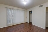 This single-floor unit offers a well-organized layout that maximizes its compact footprint. The main room features rich, dark hardwood-style flooring that runs throughout the space, neutral wall tones, and a textured ceiling with a ceiling fan and light fixture. A large floor-to-ceiling vertical blind-covered window fills the room with natural light and offers a pleasant outdoor view of green surroundings. Two closets provide ample storage, each with built-in shelving and hanging rods, conveniently accessible from the main living area. A bonus room adds flexibility to the layout and is equipped with a stainless steel mini-refrigerator and microwave, along with additional closet storage and direct access to the bathroom. The bathroom is well-appointed with a granite-style countertop vanity, dark espresso cabinetry with brushed nickel hardware, a large mirror, and a full tub-and-shower combination with white tile surround. Consistent hardwood-style flooring extends into the bathroom, tying the space together cohesively. HVAC vents are present throughout, ensuring climate control across all areas. This space is practical, clean, and thoughtfully designed for efficient everyday living.