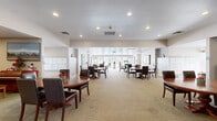 This single-floor community center in Antioch, California, offers a well-organized and functional layout designed to accommodate a variety of social activities. The entrance features a striking arched glass doorway that floods the foyer with natural light, creating an inviting first impression. Adjacent to the entry, a bulletin board and seating area provide a convenient space for residents to gather information and connect.

The expansive main hall serves as the heart of the facility, furnished with multiple round wooden dining tables and dark leather chairs arranged throughout the carpeted space. Recessed lighting illuminates the room evenly, while large windows at the far end allow natural light to filter in. Built-in mailbox units line the walls, adding a practical community element to the space.

A separate lounge area offers a more relaxed atmosphere, featuring comfortable upholstered seating, built-in bookshelves, a large flat-screen television, and a decorative fireplace that serves as the room's focal point.

The game room extends the facility's recreational offerings, housing a full-sized billiards table alongside additional dining seating and another television setup. Sliding glass doors provide access to an outdoor area, enhancing the overall flow and connectivity of the space.