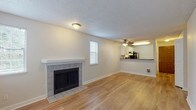 This single-floor residence offers a thoughtfully designed layout that balances open living spaces with comfortable private areas. The living room serves as the heart of the home, centered around a classic tile-surround fireplace with a clean white mantel. Light wood-style flooring extends throughout the main living areas, reflecting natural light that filters in through multiple windows dressed with white blinds. A textured ceiling and ceiling fan add both character and practicality to the space.

The kitchen is open to the living area via a pass-through counter with a dark countertop, creating a connected, social atmosphere. White shaker-style cabinetry provides ample storage, while stainless steel appliances — including a refrigerator, range, and dishwasher — offer modern functionality. The kitchen also features matching light wood-style flooring, maintaining visual continuity throughout.

The bedroom is a serene retreat, finished with soft neutral carpet and a baseboard heater beneath a window that brings in natural light. The full bathroom is clean and efficient, featuring a white vanity with modern hardware, a mirror, and a tub-shower combination with white tile surround. The space as a whole presents a cohesive, move-in-ready environment with a neutral palette throughout.