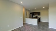 This single-floor space showcases a clean, open-concept design that seamlessly connects the living area to the kitchen. The kitchen is a standout feature, equipped with stainless steel appliances including a refrigerator, electric range, and over-the-range microwave. Dark espresso-toned cabinetry provides strong visual contrast against the light gray walls, while granite countertops add a touch of sophistication. A white peninsula extends into the living space, offering additional counter space and serving as a natural divider between the two areas. The peninsula also features an integrated sink, enhancing both functionality and flow. Recessed lighting throughout ensures consistent, even illumination across the space. The flooring is composed of durable wood-look planks in a warm gray tone, complementing the neutral color palette of the walls and trim. Smooth white baseboards line the perimeter, contributing to the space's polished, contemporary aesthetic. The open layout and thoughtful design create a functional and visually cohesive environment suitable for everyday living.