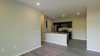 This single-floor space showcases a clean, open-concept design that seamlessly connects the living area to the kitchen. The kitchen is a standout feature, equipped with stainless steel appliances including a refrigerator, electric range, and over-the-range microwave. Dark espresso-toned cabinetry provides strong visual contrast against the light gray walls, while granite countertops add a touch of sophistication. A white peninsula extends into the living space, offering additional counter space and serving as a natural divider between the two areas. The peninsula also features an integrated sink, enhancing both functionality and flow. Recessed lighting throughout ensures consistent, even illumination across the space. The flooring is composed of durable wood-look planks in a warm gray tone, complementing the neutral color palette of the walls and trim. Smooth white baseboards line the perimeter, contributing to the space's polished, contemporary aesthetic. The open layout and thoughtful design create a functional and visually cohesive environment suitable for everyday living.