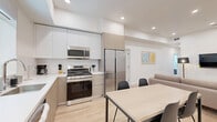 Located at 626 N Wilton Place in the heart of Los Angeles, this thoughtfully designed unit offers five private bedrooms, each with its own dedicated bathroom, making it ideal for shared living arrangements. The interior is characterized by a clean, modern aesthetic featuring light wood-style flooring, crisp white walls, and recessed lighting throughout.

The open-plan kitchen and dining area serves as a central hub of the unit, showcasing two-tone cabinetry in white and warm taupe, white quartz countertops, stainless steel appliances including a gas range, built-in microwave, dishwasher, and a full-size refrigerator. A window above the sink fills the kitchen with natural light. A dining table with seating for four completes the space.

The living room is bright and welcoming, with recessed lighting, a wall-mounted television, and direct access to an in-unit laundry area equipped with a full-size washer and dryer — a notable convenience.

Each bedroom is compact yet functional, featuring sliding closet doors, light flooring, and smart lock-enabled entry doors for added privacy and security. The bathrooms are uniformly finished in all-white tile with tub-shower combinations, offering a clean and cohesive look. The overall ambiance is modern, minimal, and highly functional.