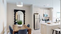 Located at 98 Northwood Blvd in Pittsboro, NC, this well-appointed 2-bedroom, 2-bathroom single-floor residence offers a thoughtfully designed open-concept layout filled with natural light. Light wood-style flooring flows throughout the main living areas, creating a clean, cohesive aesthetic.

The kitchen is a standout feature, boasting a large center island with a double sink, crisp white quartz countertops, light-toned cabinetry with matte black hardware, and stainless steel appliances including a refrigerator, range, microwave, and dishwasher. Pendant lighting above the island adds a polished touch. The kitchen opens seamlessly into both the dining area and the living room.

The dining area accommodates a full dining table and is accented by a modern pendant light. The bright living room features a ceiling fan, large windows with blinds, and a glass door leading to a private balcony.

The spacious primary bedroom offers plush carpet, a ceiling fan, natural light from large windows, and generous proportions. The second bedroom is equally comfortable with carpeted flooring and ample natural light. Both bathrooms are finished with white cabinetry, large vanity mirrors, and glass-enclosed showers. A walk-in closet with wire shelving provides convenient storage.