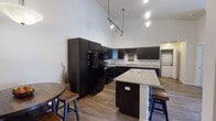 Located at 3202 Market Ln in Kenosha, WI, this single-floor residence offers a thoughtfully designed layout with a variety of functional and stylish living spaces. The kitchen is a standout feature, showcasing dramatic vaulted ceilings, espresso-toned cabinetry, black appliances, and striking granite countertops that extend across a central island with bar seating — ideal for both cooking and casual dining. A built-in wine rack and tile backsplash add refined detail, while wood-look flooring and track lighting contribute to the modern aesthetic. The dining area sits adjacent to the kitchen, providing a seamless flow for entertaining. The living room offers a comfortable, open feel with hardwood-style flooring, neutral walls, and direct access to additional rooms. Bedrooms are carpeted and feature vaulted or angled ceilings, with natural light streaming through wide windows with blinds. One bedroom includes a built-in bunk bed configuration, offering flexible use. The bathroom is clean and functional, featuring a walk-in shower, dark vanity with light countertop, and tile flooring. A dedicated laundry area is also visible within the unit. Throughout, the space maintains a cohesive, contemporary style with neutral tones and quality finishes.