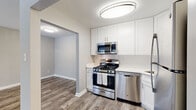 This well-appointed single-floor residence showcases a thoughtful layout with modern finishes throughout. The kitchen is a standout feature, equipped with crisp white shaker-style cabinetry, bright white quartz countertops, and a classic subway tile backsplash. Stainless steel appliances — including a gas range, over-the-range microwave, dishwasher, and refrigerator — complete the space, which is illuminated by a contemporary oval flush-mount light fixture. Wood-style plank flooring runs throughout the main living areas, lending warmth and continuity to the open-concept design. The living area is bright and welcoming, highlighted by a sliding glass door that opens to a private balcony with views of surrounding greenery, allowing natural light to fill the room. The bedrooms are finished with plush carpeting and feature ample closet space, including a built-in rod and shelf system. Neutral gray tones on the walls create a calm, cohesive palette throughout. The bathroom is finished with white subway tile in a clean walk-in shower, complemented by a white vanity and brushed nickel fixtures. The overall ambiance is modern, clean, and move-in ready, with a balanced combination of updated design elements and functional living spaces.