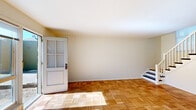 This two-floor space is defined by its consistent use of parquet hardwood flooring, which runs throughout the main living areas and upper-level rooms, adding warmth and visual texture to each space. The main level features a generously sized living area bathed in natural light, thanks to a large picture window and sliding glass door that open to an outdoor greenspace, creating a seamless indoor-outdoor connection. A secondary entry door with glass panel detailing provides additional access and further enhances the brightness of the lower level. A staircase with a white-painted banister connects the two floors, providing a clean, classic transition point within the space.

The kitchen is thoughtfully laid out with white cabinetry, wood-toned countertops, a white gas range, and a refrigerator, complemented by a window that draws in natural light. The gray tile flooring in the kitchen offers a practical contrast to the parquet found elsewhere. The upper level continues the parquet flooring into the bedrooms, each featuring neutral walls and ample natural light from well-positioned windows. The bathroom is finished with gray square tile surrounding the tub and shower area, a wall-mounted mirror, and clean white fixtures. Throughout, the space maintains a bright, neutral palette that lends itself to a variety of uses.
