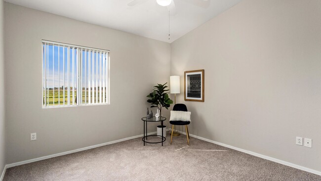 Dormitorio con alfombra suave y neutra, ventilador de techo de varias velocidades y una ventana con luz solar. - Riverwood Apartments