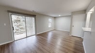 This one-bedroom, one-bathroom apartment at Woodhaven Park Apartments in Indianapolis, Indiana offers a practical and comfortable single-floor layout. The combined kitchen and living area forms the heart of the unit, featuring warm hardwood-style flooring that extends throughout the main living spaces. The living room is bright and open, with a large sliding glass door dressed in vertical blinds that allows natural light to fill the room and provides a view of the surrounding greenery. A secondary window further enhances the light and airy feel of the space. The kitchen is separated from the living area by a half-wall with a pass-through shelf, creating a semi-open layout. It is equipped with dark cabinetry and a full-size refrigerator. The bedroom is a well-proportioned room featuring plush carpeting, a window with outdoor views, and access to a spacious walk-in closet outfitted with full-length hanging rods and additional carpet flooring. The bathroom includes a full tub-shower combination, a dark-finished vanity with an integrated sink, and wood-style flooring that ties in with the rest of the unit. Neutral gray tones on the walls throughout the apartment create a clean, cohesive aesthetic.