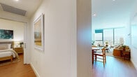 Located on a high floor along Wilshire Boulevard in Los Angeles, this 2-bedroom, 2-bathroom residence offers a sleek, contemporary living experience defined by abundant natural light and sweeping panoramic views of the city and surrounding mountains. Light wood flooring flows throughout the open-concept layout, connecting the living, dining, and kitchen areas seamlessly. The living room is anchored by floor-to-ceiling windows that frame striking cityscape views, while the open kitchen features flat-front cabinetry in soft neutral tones, stainless steel appliances, and clean white countertops, complemented by a round wood dining table ideal for casual meals. The primary bedroom is a bright, airy retreat with expansive window walls offering commanding views, and its en-suite bathroom showcases large-format tile flooring, a glass-enclosed walk-in shower, and a floating vanity. The second bedroom similarly benefits from generous glazing and city views. A dedicated hallway and closet provide practical storage. Clean white walls, recessed lighting, and a consistently modern aesthetic give the entire residence a refined, understated ambiance well-suited to urban living in the heart of Los Angeles.