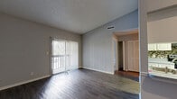 Located at 9101 Avenue Club Drive in Tampa, FL, this one-bedroom, one-bathroom unit offers a practical and comfortable single-floor layout. The combined kitchen and living area serves as the heart of the home, with dark hardwood-style flooring running throughout and a textured ceiling overhead. The living room receives natural light through a large sliding glass door fitted with vertical blinds, offering outdoor views. A pass-through window connects the kitchen to the living area, creating an open, connected feel. The kitchen features white cabinetry, a mosaic tile backsplash, stone-toned countertops, and black appliances including a range and refrigerator, all set on wood-look flooring. The bedroom is carpeted for comfort, features neutral gray walls, a textured ceiling, and a window with vertical blinds that brings in natural light. It includes access to a dedicated walk-in closet outfitted with dual wire shelving racks and carpeted flooring, providing generous storage. The bathroom offers a full tub-shower combo with tiled surround, white vanity cabinetry, a gray countertop, a large mirror, and wood-look flooring. The overall aesthetic throughout is clean and contemporary, with a consistent gray and white color palette.