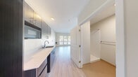 Located at 8500 20th Ave NE in Seattle's Wedgwood neighborhood, this efficiently designed single-floor unit offers a thoughtful layout across its compact footprint. The open living area is anchored by a triple-panel window that floods the space with natural light and provides views of the surrounding neighborhood. Light wood-toned vinyl plank flooring runs throughout, lending a clean, contemporary aesthetic to the interior.

The kitchenette is outfitted with dark espresso-finish cabinetry — both upper and lower — paired with a light quartz countertop and a stainless steel sink. A built-in microwave and space for a compact refrigerator complete the functional cooking area. The neutral white walls and recessed lighting keep the space feeling bright and open.

A closet with a full-width hanging rod provides dedicated storage, accessible directly from the main living area. The bathroom features a clean, utilitarian design with cork-toned flooring, a toilet, sink, and shower, along with accessibility-friendly grab bars and towel fixtures. The overall design of the unit prioritizes functionality and modern simplicity, making it a practical and well-appointed space in the heart of Seattle's established Northeast neighborhood.