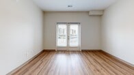 This single-floor, one-bedroom, one-bathroom unit in Wichita, KS (67206) offers a functional and modern layout with consistent warm-toned hardwood-style flooring throughout. The combined kitchen and living area forms the heart of the unit, where a well-equipped kitchen showcases rich dark wood cabinetry, light granite-style countertops, and a full suite of stainless steel appliances, including a refrigerator, dishwasher, range, and over-the-range microwave. Recessed lighting illuminates the kitchen, complementing the open feel of the adjoining living space. The living area benefits from natural light streaming through French doors that open to a private balcony, offering outdoor views and a welcoming indoor-outdoor connection. The bedroom is a comfortably sized retreat with a window that brings in additional natural light and neutral walls that offer a clean, versatile canvas. The bathroom mirrors the cohesive design of the unit, featuring a warm wood vanity with a granite-style countertop and hardwood-style flooring. Throughout the unit, crisp white walls and clean lines create a bright, minimalist ambiance that maximizes the sense of space.