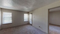 This single-story residential unit offers a practical and comfortable layout designed for everyday living. The living area serves as the heart of the home, featuring wall-to-wall carpeting, neutral-toned walls, and a textured ceiling that adds dimension overhead. A front entry door opens directly into this space, which is brightened by a window fitted with horizontal blinds. An adjacent area provides a seamless transition to the kitchen and bedroom, all connected via a central hallway.

The kitchen is a functional galley-style space finished with rich, dark espresso cabinetry and light-toned countertops. A mosaic tile backsplash adds a decorative accent, while the kitchen comes equipped with black appliances including a refrigerator, electric range, and over-the-range microwave. Wood-look flooring runs throughout the kitchen and bathroom areas, providing a durable contrast to the carpeted rooms.

The bedroom is a well-proportioned, quiet retreat with soft carpeting underfoot and a large window that invites natural light and outdoor views. An additional room with its own window and private access door offers flexible use as a second bedroom or den.

The bathroom features a clean, white tub and shower combination with tiled surrounds, complemented by the same wood-look flooring found in the kitchen, creating a cohesive aesthetic throughout the unit.