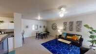 This single-floor residence offers a thoughtfully designed layout that balances comfort and functionality across its key living spaces. The open-plan living and dining area serves as the heart of the home, featuring plush carpeting, a neutral color palette, and ample room for both relaxing and entertaining. The living area accommodates a sofa and coffee table, while the adjacent dining space comfortably seats four. Together, they create a cohesive, inviting atmosphere.

The kitchen is well-equipped with white cabinetry extending to the ceiling, dark countertops, tile flooring, and a full suite of appliances including an electric range, overhead microwave, and sink — providing generous storage and prep space.

The residence includes multiple bedrooms, each finished with carpet flooring and neutral walls. One bedroom features a ceiling fan and a window that allows natural light to filter in, along with space for a desk. Another bedroom offers a quieter, cozier setting with warm lamp lighting.

Two full bathrooms serve the home, each featuring a single-sink vanity with a large mirror, overhead lighting, and a shower-tub combination. A dedicated laundry room with tile flooring and washer hookups adds everyday convenience, rounding out this practical and comfortable living space.
