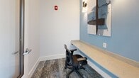 Located at 2300 The Reserve Circle in Apopka, Florida, this single-floor office suite offers a thoughtfully designed workspace configured around a central hallway and four individual office nooks. The layout is efficient and purposeful, making excellent use of its compact footprint.

The central hallway sets the tone for the space with its crisp white walls, soft blue accent panels, and light tile flooring that guides occupants to each office. Wall-mounted sconce lighting adds a polished touch, while framed abstract artwork lends a sophisticated, professional ambiance. A glazed exit door at the end of the corridor allows natural light to filter in, brightening the passage.

Each of the four offices shares a consistent and cohesive design language. Built-in stone-surfaced desks extend along the blue-painted accent walls, providing ample workspace for individual users. Ergonomic task chairs accompany each station, and stylish sconce lighting illuminates each nook with a warm, focused glow. Patterned, multi-tonal carpeting grounds each space, adding texture and visual interest underfoot. Curated abstract artwork adorns the walls of every office, reinforcing the modern aesthetic throughout.

The overall atmosphere is calm and professional, making this suite well-suited as a co-working or resident business center. The consistent use of blue and white tones, quality finishes, and purposeful lighting creates a focused yet inviting environment for productivity.