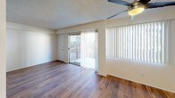 This single-story unit is laid out in a practical, connected floor plan with hardwood flooring running consistently throughout the living areas, bedrooms, and kitchen. The living room is a generous, open space anchored by a ceiling fan and fitted with large sliding glass doors that lead to an outdoor balcony, allowing natural light to fill the room. Vertical blinds on both the sliding doors and adjacent windows provide adjustable light control. A partial wall separates the living area from the kitchen, maintaining an open feel while defining each space.

The galley-style kitchen is efficiently designed, featuring white cabinetry extending to the ceiling for ample storage, dark granite-style countertops, a double stainless steel sink, and stainless steel appliances including a refrigerator, dishwasher, and range. The bedrooms are well-proportioned, each with hardwood floors, textured ceilings, and windows with vertical blinds that invite natural light. One bedroom includes a closet with louvered doors and direct hallway access. The bathroom is cleanly appointed with a white vanity, dark countertop, framed mirror, and a shower-tub combination, maintaining the consistent neutral palette found throughout the unit.
