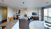 This single-floor residence showcases a thoughtfully designed open-concept layout with a contemporary aesthetic. The living room is anchored by a large sectional sofa and floor-to-ceiling windows that flood the space with natural light and offer leafy outdoor views, creating a bright and inviting atmosphere. A curated gallery wall adds a polished, artistic touch.

The open layout flows seamlessly into the dining area, which features a round wood table with modern seating, and into the living space where dark hardwood flooring provides a rich contrast to the neutral walls. Track lighting highlights the space effectively.

The kitchen is well-equipped with stainless steel appliances, white cabinetry reaching to the ceiling, granite countertops, and a subway tile backsplash — combining practicality with clean, modern styling.

The primary bedroom is distinguished by a bold geometric accent wall, plush carpeting, and large windows with outdoor views. A sitting area with its own window adds extra comfort and functionality.

Additional bedrooms are generously sized with soft carpeting, ample natural light, and access to well-appointed bathrooms. Each bathroom features granite-topped vanities, subway tile surrounds, soaking tubs, and neutral taupe walls, maintaining a consistent, refined design language throughout.