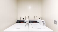 Located at 1223 Federal Ave in the West Los Angeles neighborhood of Los Angeles, CA, this shared laundry facility offers a practical and efficiently organized space for residents. The room is compact yet thoughtfully arranged, housing multiple commercial-grade Speed Queen top-load washers and dryers that are built for high-frequency use. The machines are equipped with APS digital payment systems, providing a convenient coin-free laundry experience.

The interior features neutral, light-colored walls that contribute to a clean and bright atmosphere. The flooring transitions between areas, with wood-look vinyl planks visible near the entryway, lending a modest touch of warmth to the utilitarian space. A clearly marked fire extinguisher is mounted on the wall, reflecting a commitment to safety standards.

The room is accessed through a dedicated door and is well-ventilated, with a vent visible above the entry. Informational signage is posted on the walls, offering usage instructions in both English and Spanish for the convenience of all residents. The overall layout is straightforward and functional, making laundry tasks efficient and accessible. This well-equipped laundry room serves as a dependable shared amenity for the building's residents.
