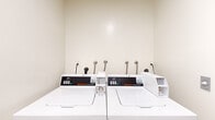 Located at 1223 Federal Ave in the West Los Angeles neighborhood of Los Angeles, CA, this shared laundry facility offers a practical and efficiently organized space for residents. The room is compact yet thoughtfully arranged, housing multiple commercial-grade Speed Queen top-load washers and dryers that are built for high-frequency use. The machines are equipped with APS digital payment systems, providing a convenient coin-free laundry experience.

The interior features neutral, light-colored walls that contribute to a clean and bright atmosphere. The flooring transitions between areas, with wood-look vinyl planks visible near the entryway, lending a modest touch of warmth to the utilitarian space. A clearly marked fire extinguisher is mounted on the wall, reflecting a commitment to safety standards.

The room is accessed through a dedicated door and is well-ventilated, with a vent visible above the entry. Informational signage is posted on the walls, offering usage instructions in both English and Spanish for the convenience of all residents. The overall layout is straightforward and functional, making laundry tasks efficient and accessible. This well-equipped laundry room serves as a dependable shared amenity for the building's residents.