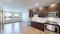 Located at 69 Arch St in Hartford, Connecticut, this modern single-floor unit offers a clean, contemporary design with quality finishes throughout. The open-concept layout seamlessly connects the kitchen and living area, creating a spacious and functional environment. Light wood-tone flooring runs throughout, complementing the bright white walls and recessed lighting that give the space a fresh, airy feel.

The kitchen is a standout feature, equipped with rich dark-brown cabinetry extending to the ceiling for ample storage, crisp white quartz countertops, a white subway tile backsplash, and a full suite of stainless steel appliances including a refrigerator, range, microwave, and dishwasher. A stainless steel undermount sink with a modern arc faucet completes the well-designed workspace.

The bedroom is generously proportioned, benefiting from dual windows that bring in abundant natural light and offer views of the surrounding neighborhood. The hallway area includes a louvered closet door and convenient access to the electrical panel.

The bathroom maintains the unit's modern aesthetic with large-format dark tile flooring, a white vanity with granite-style countertop, a lighted mirror, and a shower/tub combination. Every detail reflects a thoughtfully designed living space suited for comfortable urban living in downtown Hartford.